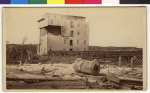 The west end of Cole's Mill was blown in, the roof blown off, the corner of a wall torn out, the machinery damaged and the cooper shop destroyed. Eight box cars were overturned and two carloads of flour were in the mill race. John M. Cole, the proprietor of the mill was found dead in the street between the mill and his residence. He had apparently left the mill to go home when he was killed by the storm. In the foreground is the leveled home of Paul Thompson, who worked for the mill and occupied a home rented from the mill. The stove is all that is recognizable of any of the house furnishings.