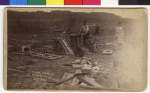 Several people are viewing the damage from the tornado. A man is standing next to a piece of furniture and a boy is sitting with a large toy horse. Among the debris on the ground is a stove, windows and an umbrella. The inscription on the photo is: "Cascade Park, 20 houses destroyed, 8 persons killed near here."