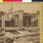 A man is leaning against a wall of the Weber's residence. Another wall lies flat on the ground and the roof is missing. 