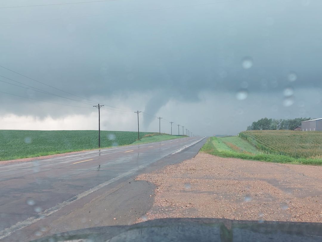 Possible tornado in the distance, contrasting from the rain shaft in the background. Road, power lines, and a field make up the foreground.