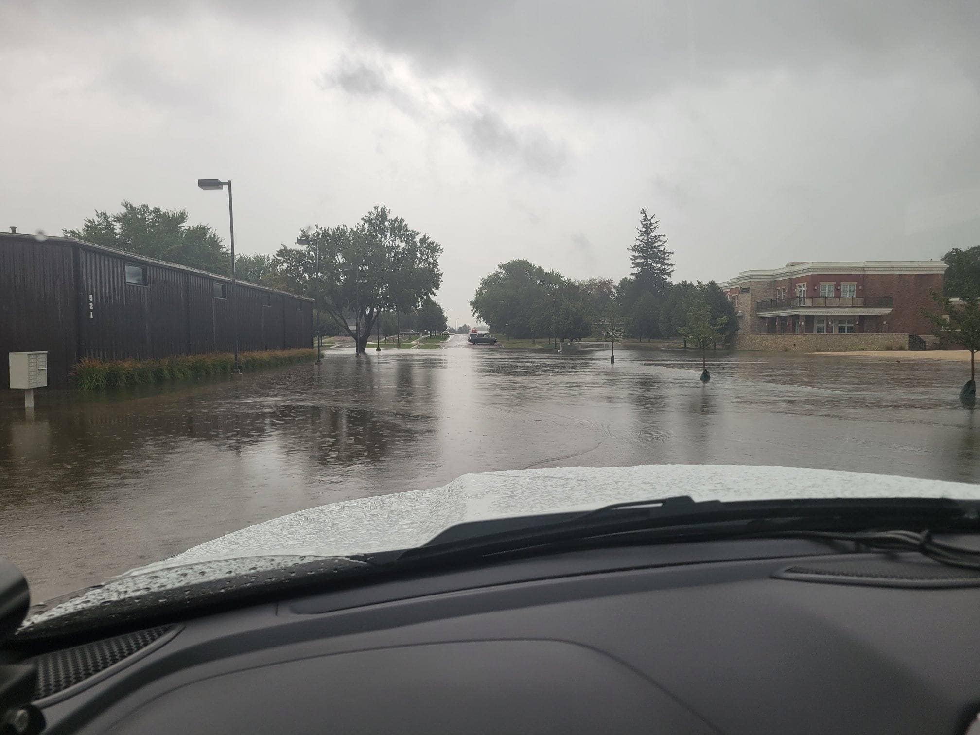 Flooded roadway in Sioux Center, Iowa, looking over the hood of a truck. In the distance, an SUV is blocking the flooded street.