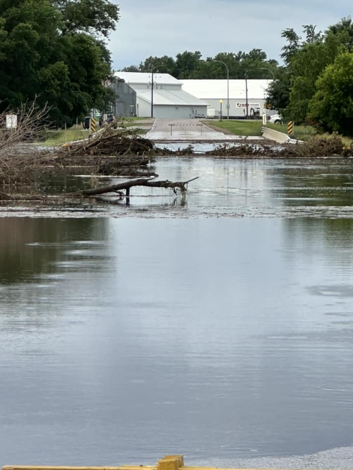 Photo of flood waters and tree debris across the road in Hospers Iowa