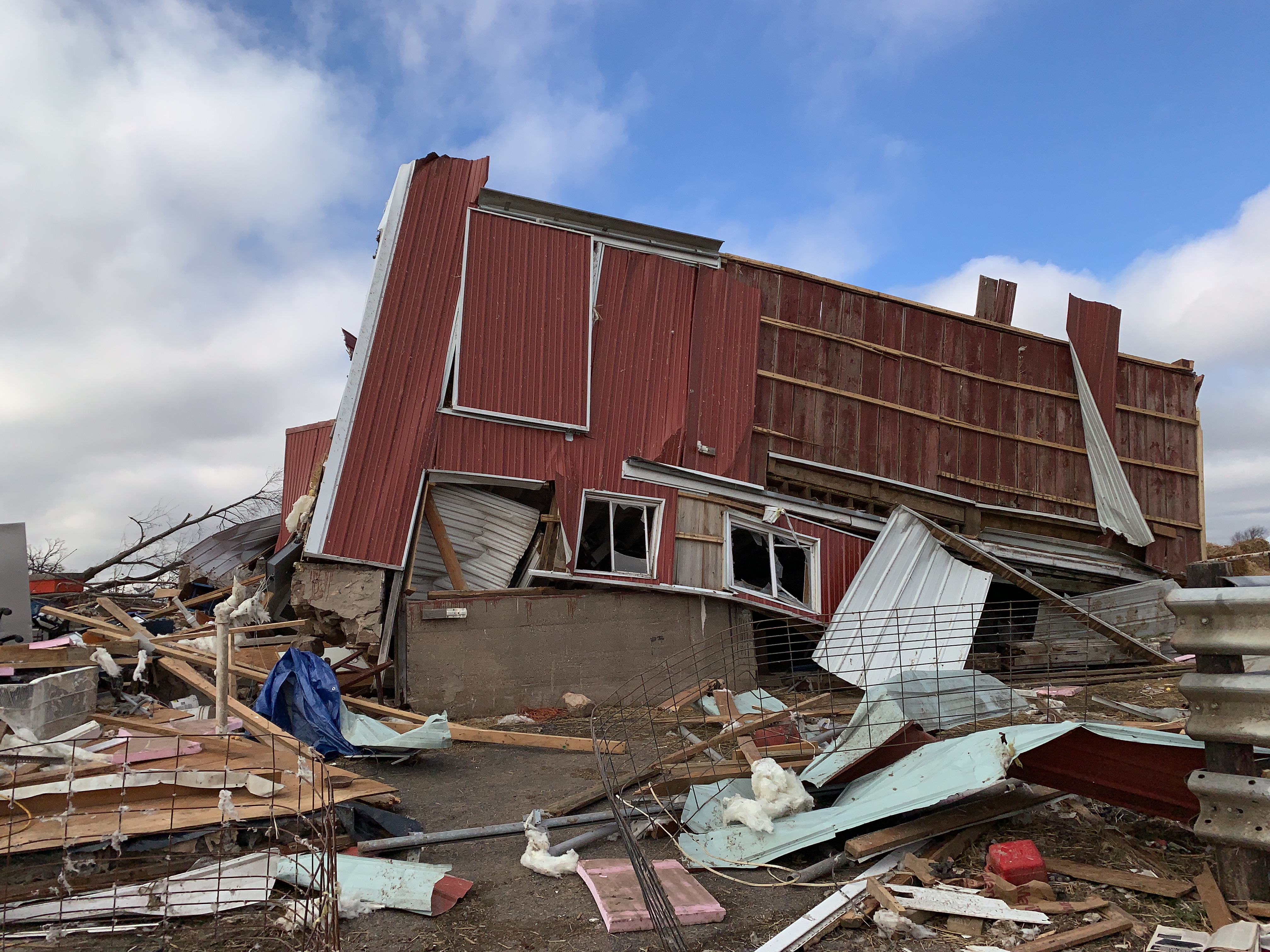 Red barn with the roof blown off or collapsed and tipped off its foundation