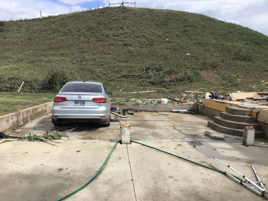  A silver sedan is parked on a concrete slab next to a grassy hill. Debris is scattered on the ground around the car and a hose is lying on the concrete.